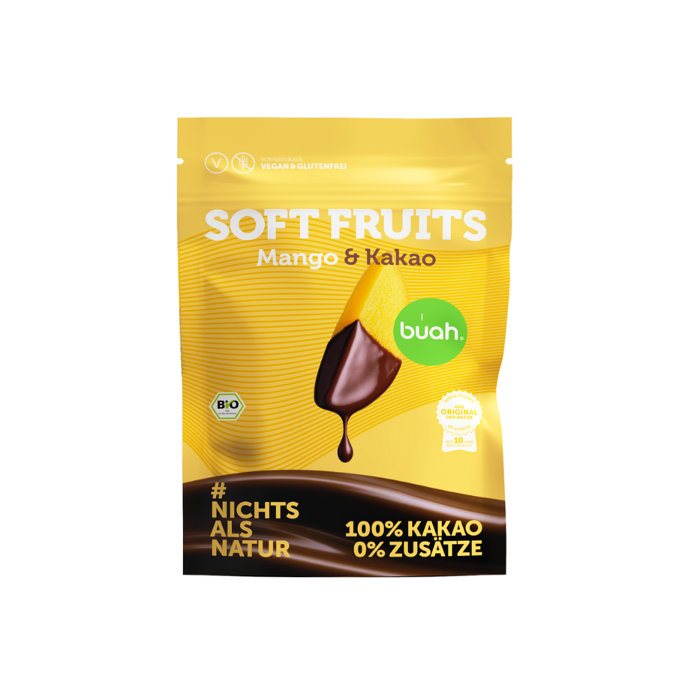 Ein gelber Beutel buah Soft Fruits der Sorte Mango & Kakao steht vor einem gelben Hintergrund. Dahinter ist die Rückseite der Verpackung zu erkennen. Davor liegen einige softe, mit Schokolade überzogene Mango-Stücke.