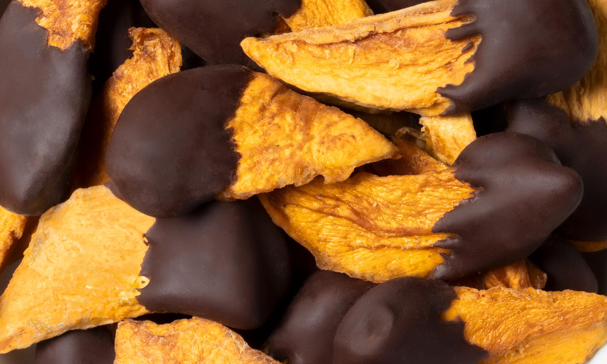 Eine Nahaufnahme von soften buah Mango-Stücken, die halb in dunkle Schokolade getaucht sind.