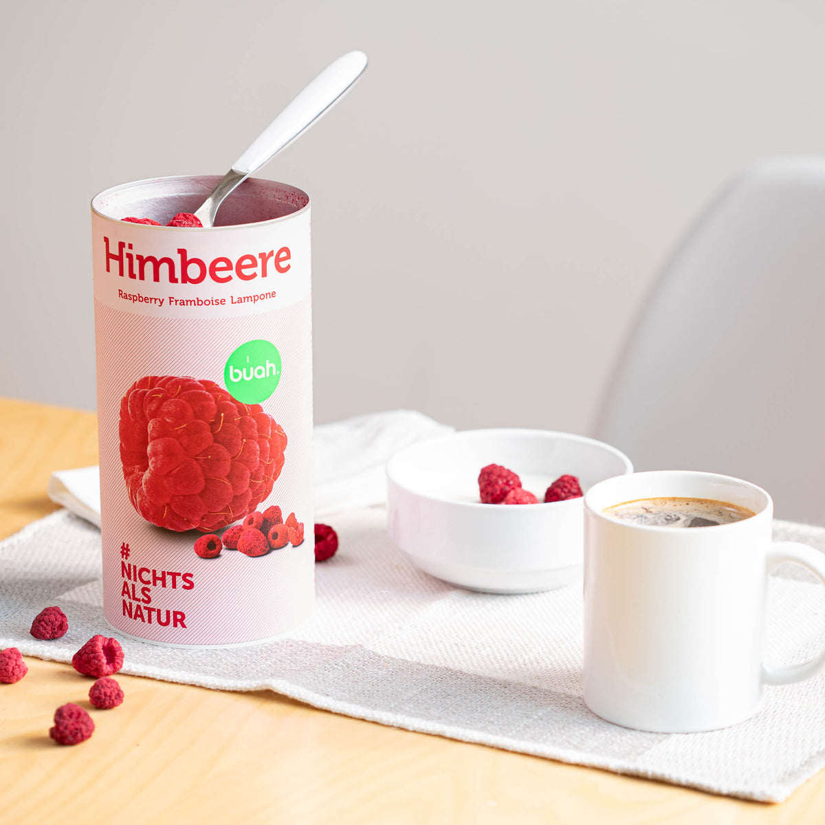 Eine Dose buah Himbeeren steht neben einer Tasse Kaffee auf dem Tisch