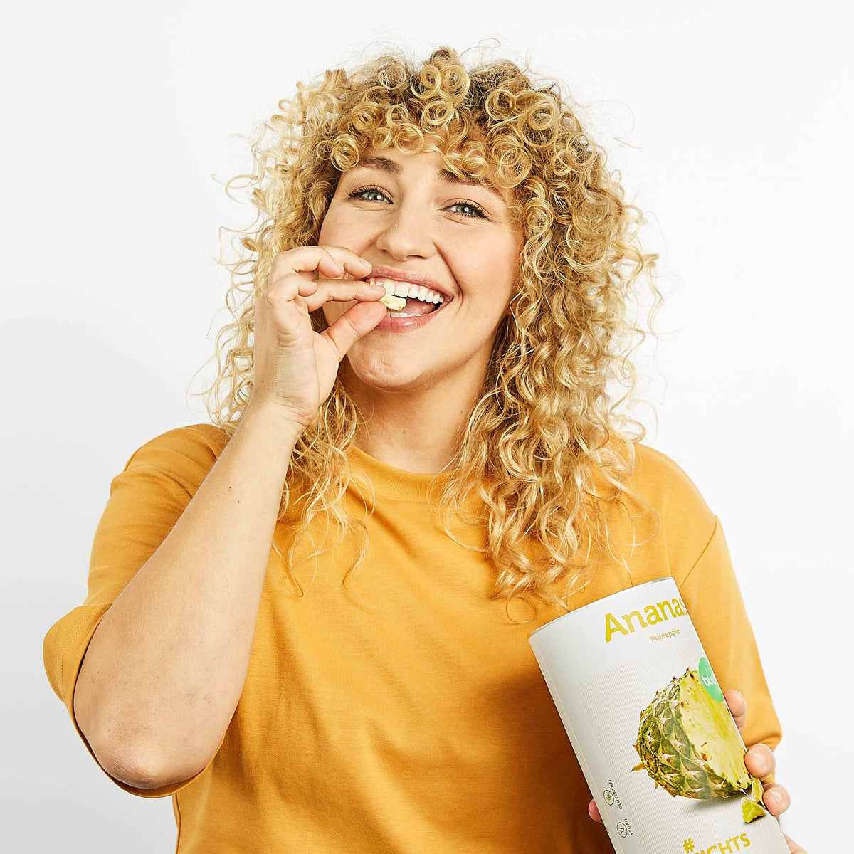 Junge Frau mit blonden Locken hat eine Dose buah Ananas in der Hand und isst nebenher gefriergetrocknete Ananas