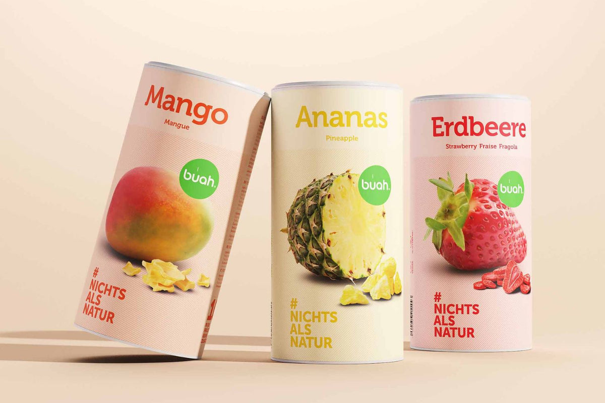 3 große buah Dosen in Zylinderform in den Sorten Mango, Ananas und Erdbeere stehen nebeneinander vor beigem Hintergrund 