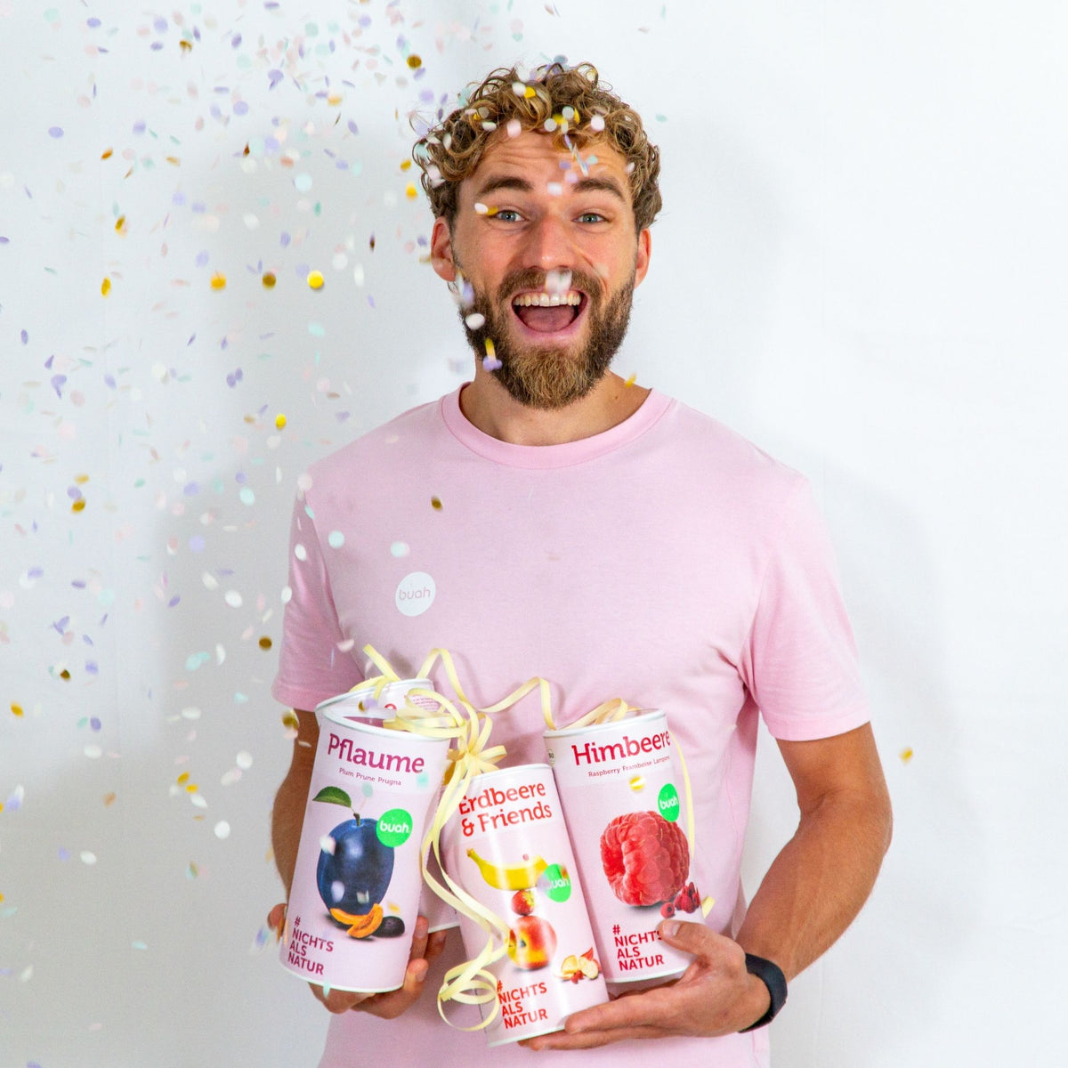 Daniel Gruender von buah in rosa buah Shirt mit buah gefriergetrockneten Fruechten in der Dose im Arm - Konfetti und Luftschlangen im Hintergrund  fuer den buah Birthday