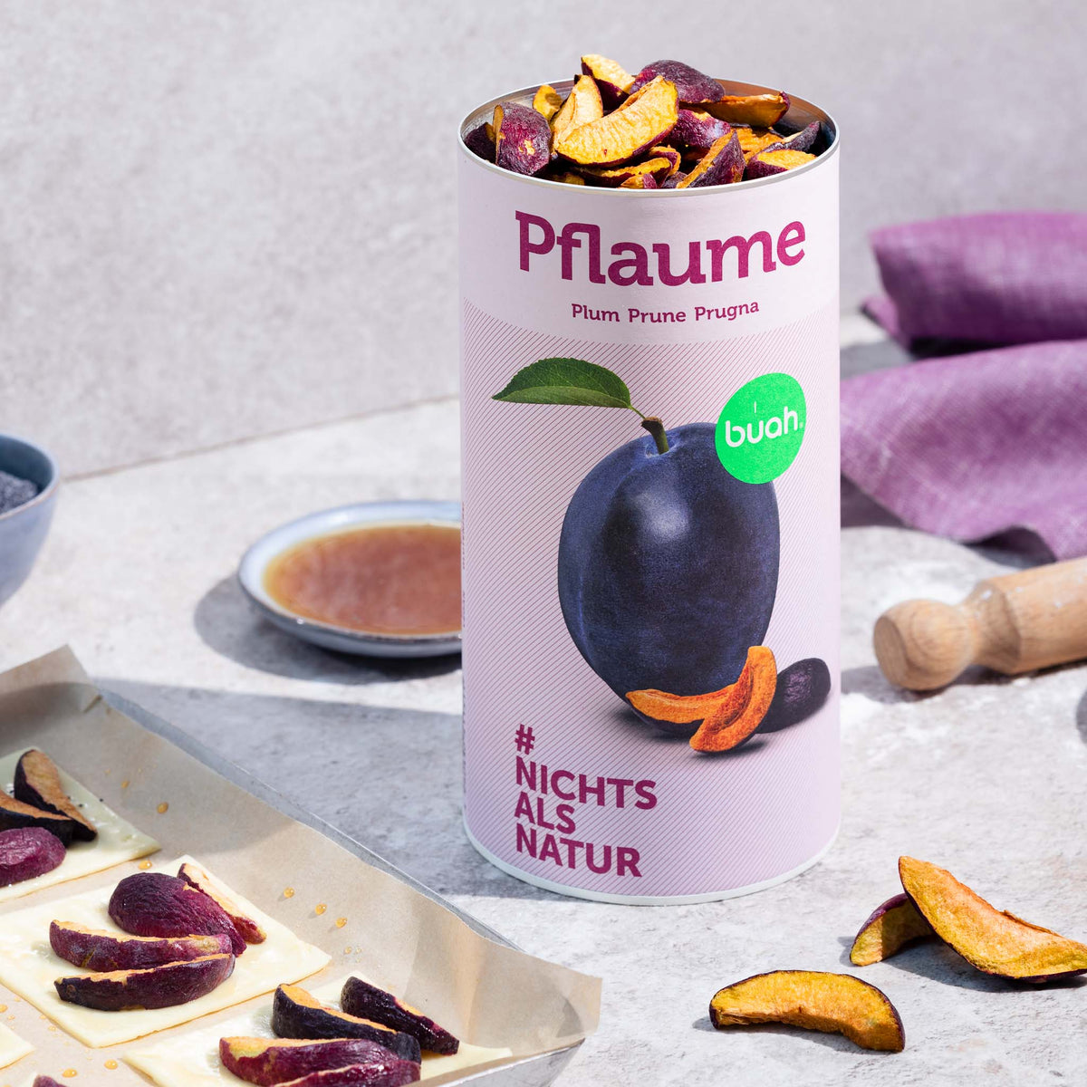 Dose buah gefriergetrocknete Pflaume steht auf einem Tisch, daneben Back-Utensilien und Pflaumen-Taschen auf einem Backblech